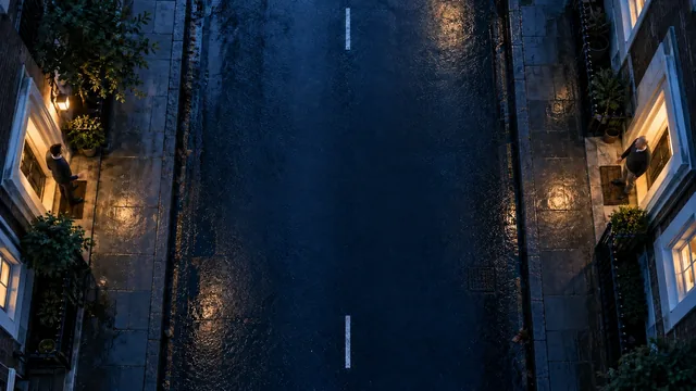 Overhead view of an empty street at night between two buildings with lit windows.